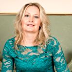 Second pic of Green dress and black lingerie blonde MILF shows off on a sofa - IamXXX.com